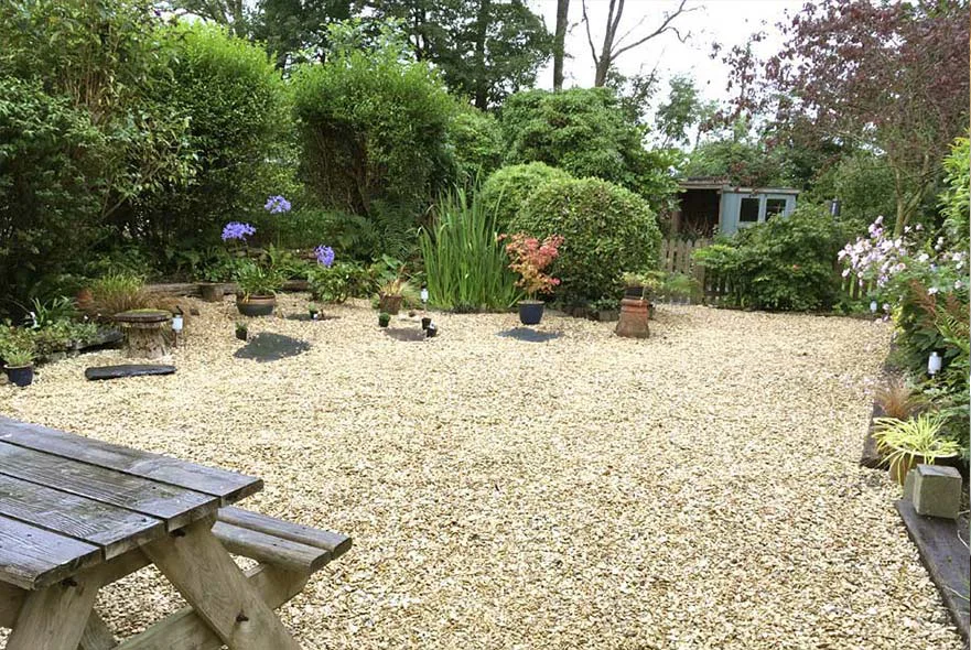 The top gravelled entertaining area of the cottage garden with a small wildlife pond and picket fence.